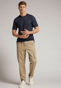 Námořnické tričko s krátkým rukávem v kombinaci s béžovými cargo kalhotami s bočními kapsami, doplněné světlými teniskami pro ležérní vzhled.