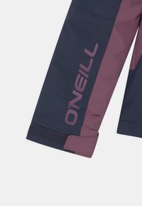 Mörkblå och kastanjefärgad isolerad jackärm med logotyp, som har en slät textur, elastiskt manschett och kontrasterande färgsättning.