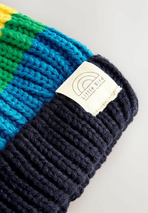 Gorro de punto con grueso ribete en amarillo, verde, azul y navy, que presenta una etiqueta blanca con un logo de arcoíris y el texto "Little Bird".