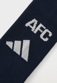 Námornícky modrá ponožka s bielym pleteným textom "AFC" a bielym trojuholníkovým dizajnom. Vyrobená z textúrovanej, elastickej tkaniny.