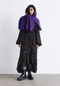 Langes schwarzes Kleid mit Blumenmuster, mit Rüschensaum, kombiniert mit einem lila, flauschigen Schal und schwarzen Plateau-Stiefeln. Glatte Stoffoberfläche mit strukturierten Akzenten.