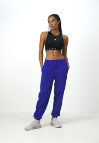 Svart sport crop top med logo og hvite aksenter, kombinert med lys blå joggebukser med slim passform og elastisk midje. Hvite sneakers.