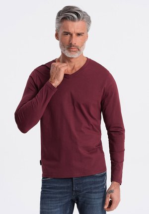 Langsleeve, bordeaux V-hals t-shirt van zacht katoen, met een zijzak en een geweven label aan de zoom, gecombineerd met blauwe jeans.