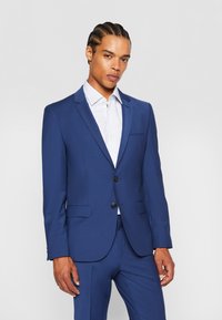 Blauw op maat gemaakt pak met een notch lapel, twee knopen en zakken. Draag het over een lichtgestreepte blouse met een soepele textuur en een moderne pasvorm.