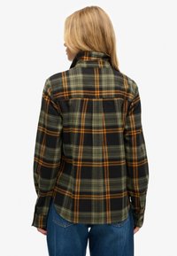 Black, green, and orange plaid flannel shirt with a high collar, long sleeves, and a curved hem, textured fabric with visible stitching.