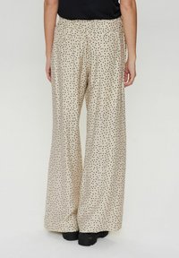 Crèmekleurige wijduitlopende broeken met een zwart stippenpatroon, voorzien van een elastische tailleband en een losse pasvorm. Er zijn twee achterzakken.