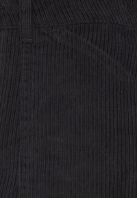 Tela de pana negra con estrías verticales, que presenta un detalle de bolsillo cosido y una textura suave, adecuada para un estilo casual.