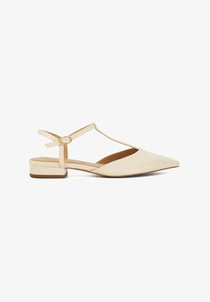 Beige T-strap flat shoes with a pointed toe, made of textured material, featuring a low block heel and a gold buckle detail on the strap.