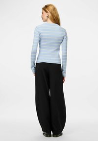 Gai zils svītrains ribots džemperis ar dzeltenām līnijām, piegulošs augšdaļa, garas piedurknes un apaļa izgriezuma kakls, kombinēts ar melnām plašām biksēm.