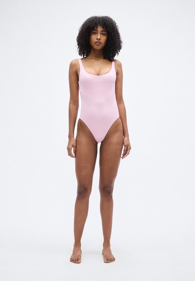 Ροζ ολόσωμο μαγιό με φαρδιές τιράντες, χαμηλή πλάτη και ψηλές περικοπές στα πόδια. Διαθέτει διακριτικό λογότυπο στο στήθος. Λείο, ελαστικό υλικό.