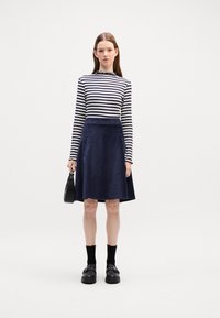 Gestreiftes langärmliges Oberteil in Marineblau und Weiß; kombiniert mit einem Marineblauen Cordrock. Schwarze Schuhe, knöchelhafte Socken und eine kleine schwarze Tasche.