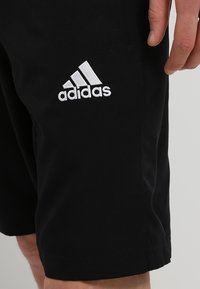 Shorts de sport noirs en tissu lisse, avec un logo Adidas brodé blanc sur le côté gauche et une coupe standard.
