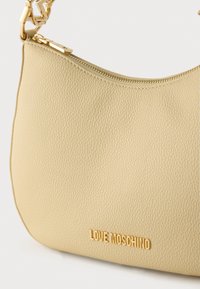Μπεζ υφασμάτινη τσάντα με χρυστό φερμουάρ και λουρί αλυσίδα, με χρυσό λογότυπο "LOVE MOSCHINO" στο μπροστινό μέρος.