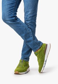 Sneaker in suede verde con suole in gomma bianche e marroni, dotate di linguetta imbottita e dettagli testurizzati. Indossate con jeans blu.