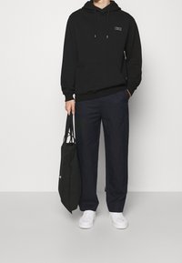 Černá bavlněná mikina s kapucí, přední kapsou a šňůrkami; spojená s námořnickými širokými kalhotami. Bílá sneakers a černá taška dotvářejí vzhled.