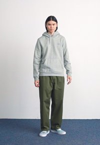 Grå hættetrøje med forlommer og ribbede manchetter, parret med løstsiddende olivengrønne bukser. Lyseblå sneakers fuldender looket.