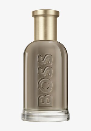 Transparente Glasflasche mit Boss-Parfüm, taupefarbener Flüssigkeit und goldfarbenem Metallverschluss, vorn mit erhabenem „BOSS“-Schriftzug.