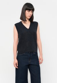 Mouwloze donkergrijze gebreide vest met een V-hals en een zachte textuur. Gecombineerd met donkerblauwe wijdvallende jeans.