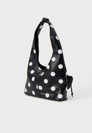 Black faux leather bag with large white polka dots. Features a slouchy design, adjustable shoulder strap, pull-string closure, and logo detail.