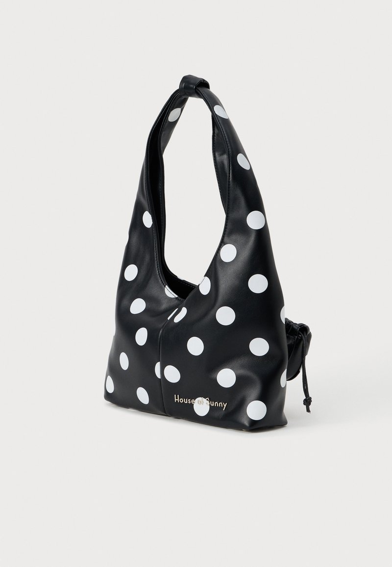 Bolsa de couro sintético preta com grandes bolinhas brancas. Apresenta um design descontraído, alça de ombro ajustável, fecho com cordão e detalhe do logótipo.