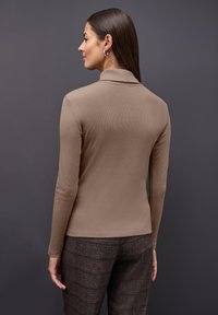 Bruine top met lange mouwen, zachte geribde textuur en een kraag, gecombineerd met donkere, patroonbroek.