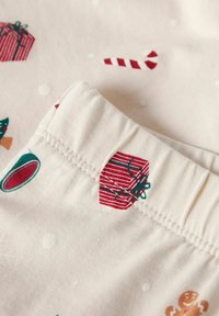 Tkanina bawełniana z jasnobeżowym tłem, pokryta czerwonymi i zielonymi wzorami świątecznymi, w tym prezentami, laskami cukrowymi i płatkami śniegu.