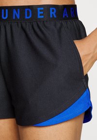 Svarta sportshorts med blå accent vid fållen. Har resår i midjan med "UNDER ARMOUR" i blå bokstäver. Mjuk, slät textur.