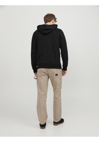 Černá mikina s kapucí a klokankou, spárovaná s béžovými cargo kalhotami s bočními kapsami a čtvercovou nášivkou na pravé noze.