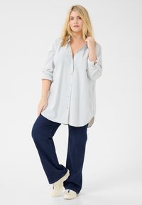 Chemise à rayures bleu clair avec une poche, associée à un jean flare bleu marine et des baskets blanches.