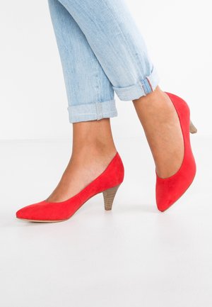 Chaussures à talons hauts en daim rouge avec un bout pointu et un talon en bois texturé, portées avec un jean denim bleu clair retroussé.
