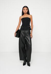 Zwarte dennen strapless top met peplum taille, gouden knoopaccenten, gecombineerd met losse zwarte leren broek en spitse zwarte haklaarzen.