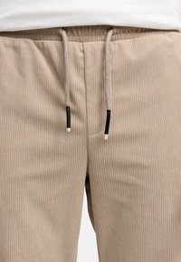 Pantaloni beige a costine con elastico in vita e coulisse, rifiniti con punte nere. Tessuto liscio con motivo a linee verticali.
