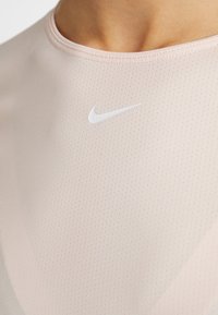 Camiseta atlética de color rosa claro con cuello redondo, tela texturizada con perforaciones y un logo de Nike blanco ubicado en el pecho.