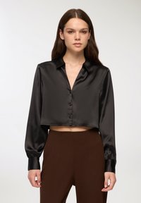 Czarna krótka bluzka z satyny z kołnierzykiem, długimi rękawami i zapinana na guziki. Gładka tekstura i subtelny połysk podkreślają jej wygląd.