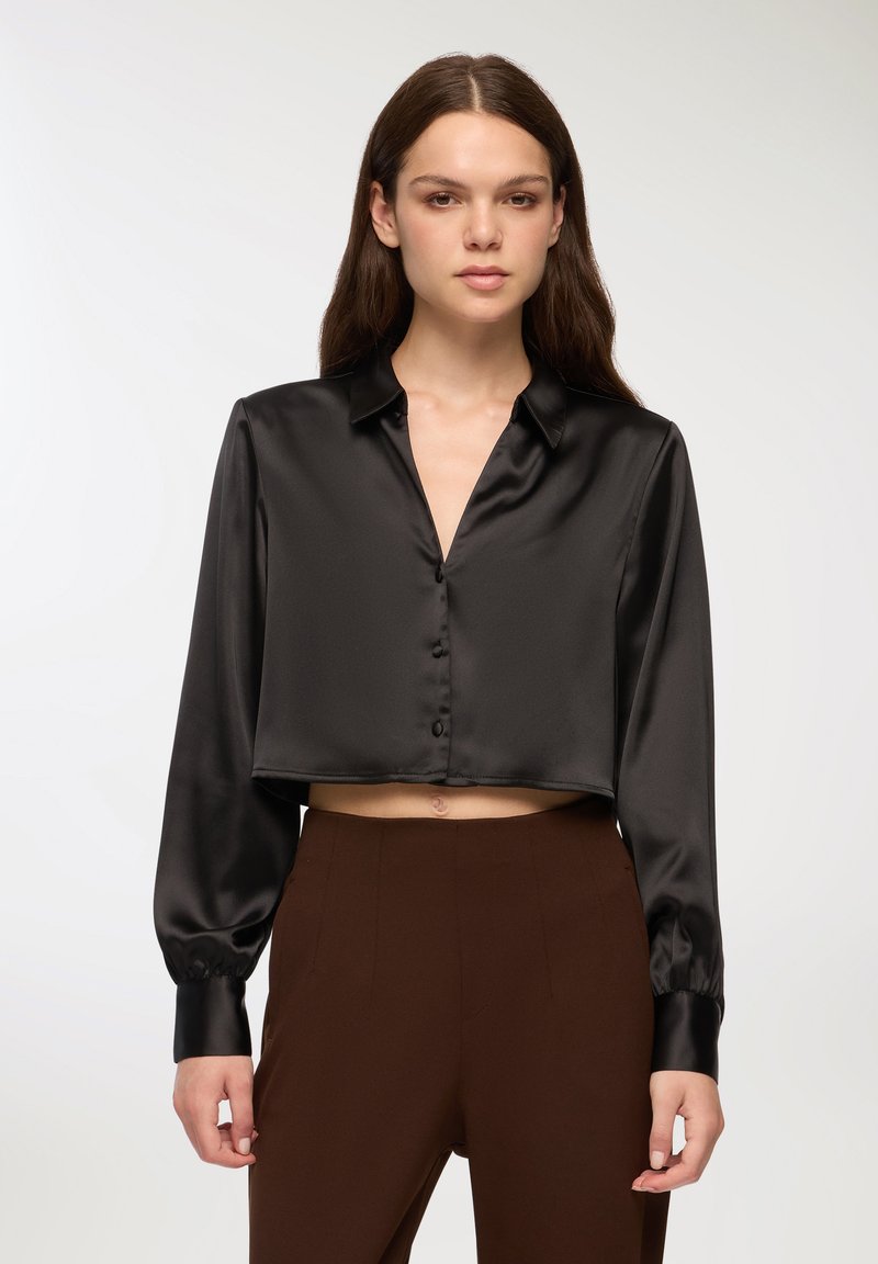 Czarna krótka bluzka z satyny z kołnierzykiem, długimi rękawami i zapinana na guziki. Gładka tekstura i subtelny połysk podkreślają jej wygląd.