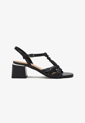 Sandale noire à talons avec un design de bride tissée, bout ouvert, sangle de cheville avec boucle et un talon carré avec un accent métallique.