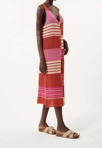 Abito senza maniche lavorato a maglia in righe arancioni, rosa e gialle; davanti con bottoni, scollatura a V, lunghezza al ginocchio. Indossato con sandali beige con fiocco.