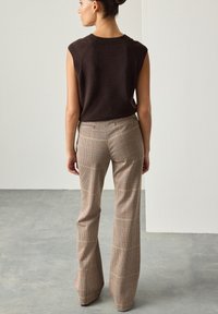 Top marrone senza maniche abbinato a pantaloni beige a quadri; i pantaloni presentano una gamba svasata e un motivo testurizzato sottile.