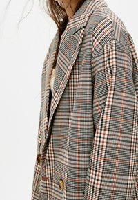 Dubbelknäppt rutigt blazer i en blandning av grå, svart, vit och rostfärgad mönster, med stora urklippta slag och knappaccentuationer.