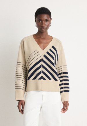 Beige V-hals trui met marineblauwe gestreepte patronen, voorzien van schuine lijnen en een relaxte fit. Zacht materiaal en iets oversized mouwen.