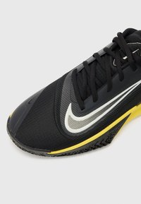 Black athletic shoe with a textured upper, featuring a white swoosh logo and yellow sole accents. Laces and mesh panels included.
