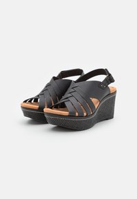 Sandales à talon noir avec des brides en cuir tressé, design à bout ouvert et plateforme en liège texturée. Comprend une bride de cheville réglable.