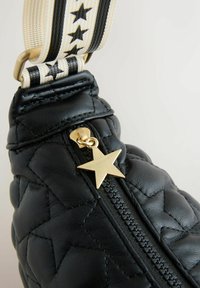 Fekete steppelt bőrtáska arany csillag alakú cipzárhúzóval, csíkos pánttal, amely fekete csillagokat mintáz krém színű alapon.