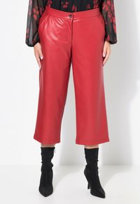 Culotte in ecopelle rossa con una forma dritta, tasche frontali e chiusura a un bottone. Abbinati a stivaletti neri aderenti alla caviglia.