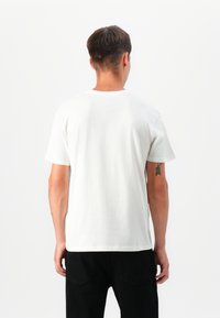 T-shirt branca de algodão com gola redonda e mangas curtas, apresentando um design simples e um ajuste padrão. Sem padrões ou detalhes notáveis.