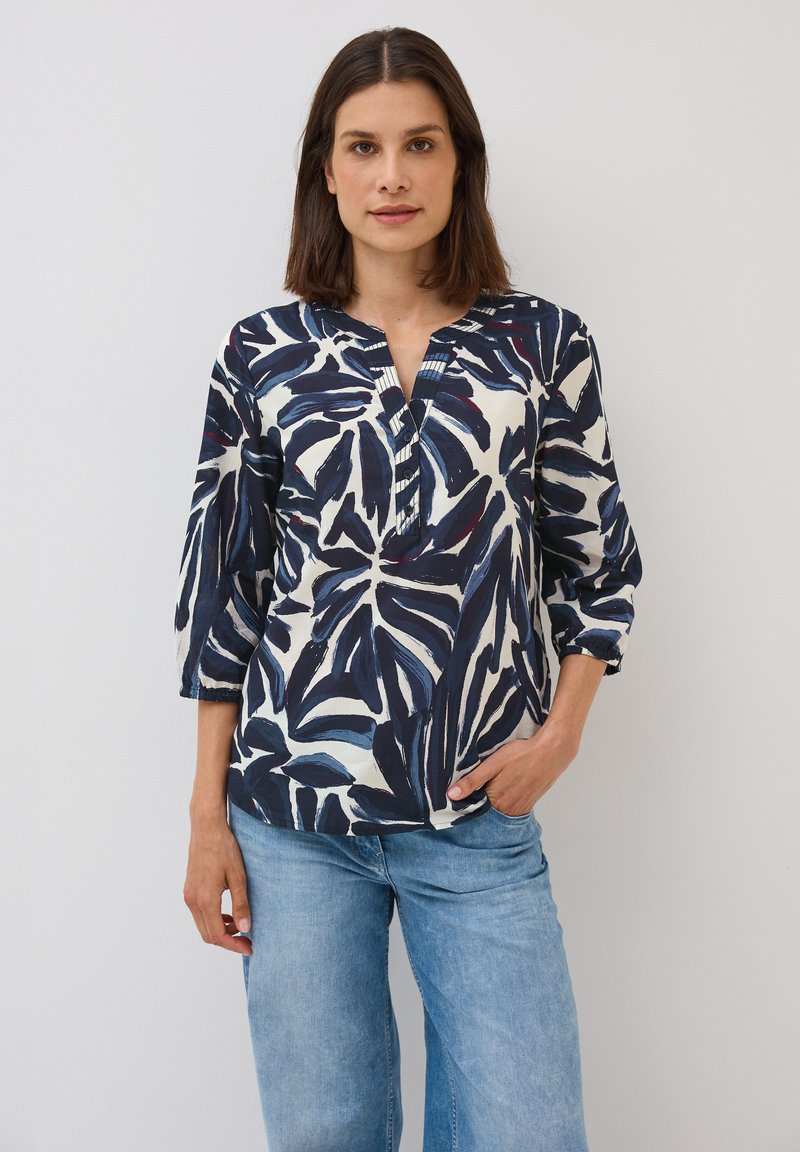 Blouse navy et crème avec un motif de feuilles, présentant un décolleté en V et des manches trois-quarts, associée à un jean large bleu clair.