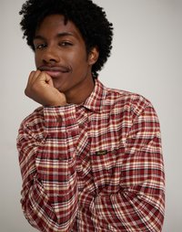 Červená a biela károvaná flanelová košeľa s hnedými gombíkmi a malým žltým logom. Obsahuje klasický golier a textúrovanú látku.