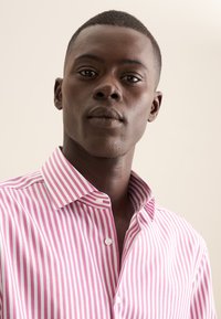 Camicia bianca a righe verticali rosa, con colletto button-down e un tessuto liscio e testurizzato. Ingrandimento sulla zona del colletto.