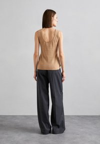 Top beige sans manches avec un dos échancré, associé à un pantalon gris ample. Le tissu semble doux avec une texture subtile.