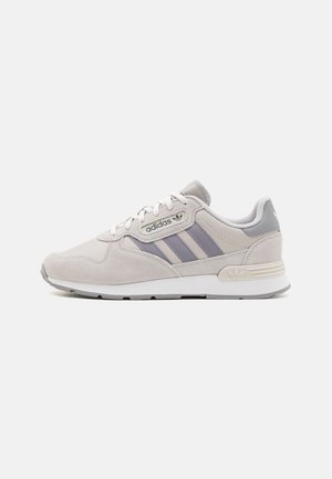 Lysegrå Adidas sneaker med tre mørkere grå striber, snøredesign og polstret sål, vist fra siden på hvid baggrund.